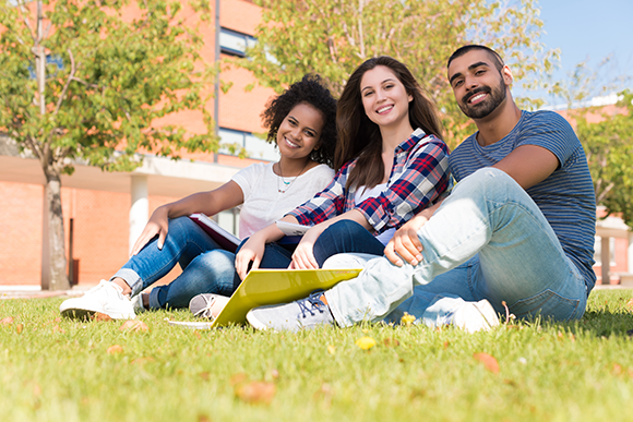 Group of students sitting on grass outside campus building